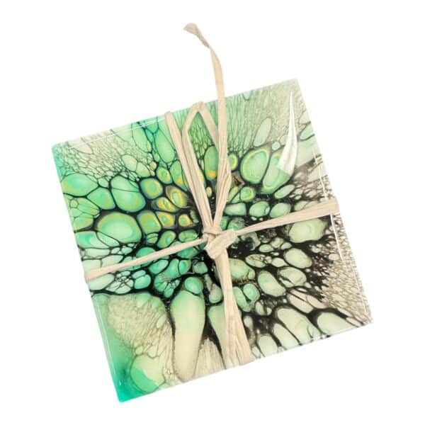 Emerald Depths) Step into a serene underwater world with May & Me's "Emerald Depths" porcelain coaster. This hand-poured creation captures the mysterious allure of the ocean's heart, using a dance of deep greens and shadowy blacks to bring an element of nature's depth to your table. Each coaster is a testament to the unique craftsmanship, where the swirling patterns offer a glimpse into the swirling waters of an untouched sea. Crafted from premium porcelain, "Emerald Depths" not only serves as a safeguard for your surfaces but also enchants as a standalone piece of art. Its durable, glossy finish ensures long-lasting beauty and functionality, making it easy to clean and resistant to the wear and tear of daily life. Whether set beneath a steamy mug or a cold glass, this coaster remains unyieldly in both form and function. Ideal for those who appreciate the artistry in the everyday, this coaster can transform any drinking experience into a moment of zen. Its cool, tranquil color palette makes it an excellent complement to modern and minimalist decor, acting as a subtle yet striking centerpiece. Gift it or keep it for yourself—either way, "Emerald Depths" promises to add a touch of elegance and mystery to your home, inviting the calm of the deep sea right to your doorstep.