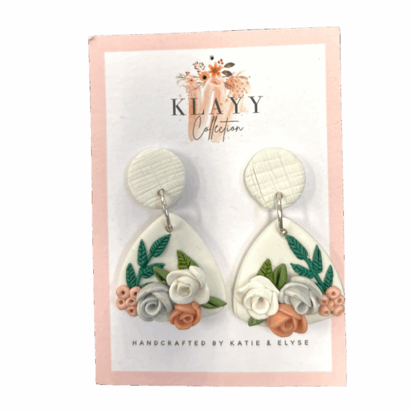 Blush Botanica earrings feature sculpted pastel roses and leaves on white teardrops with textured white studs. Soft, romantic, and handmade.