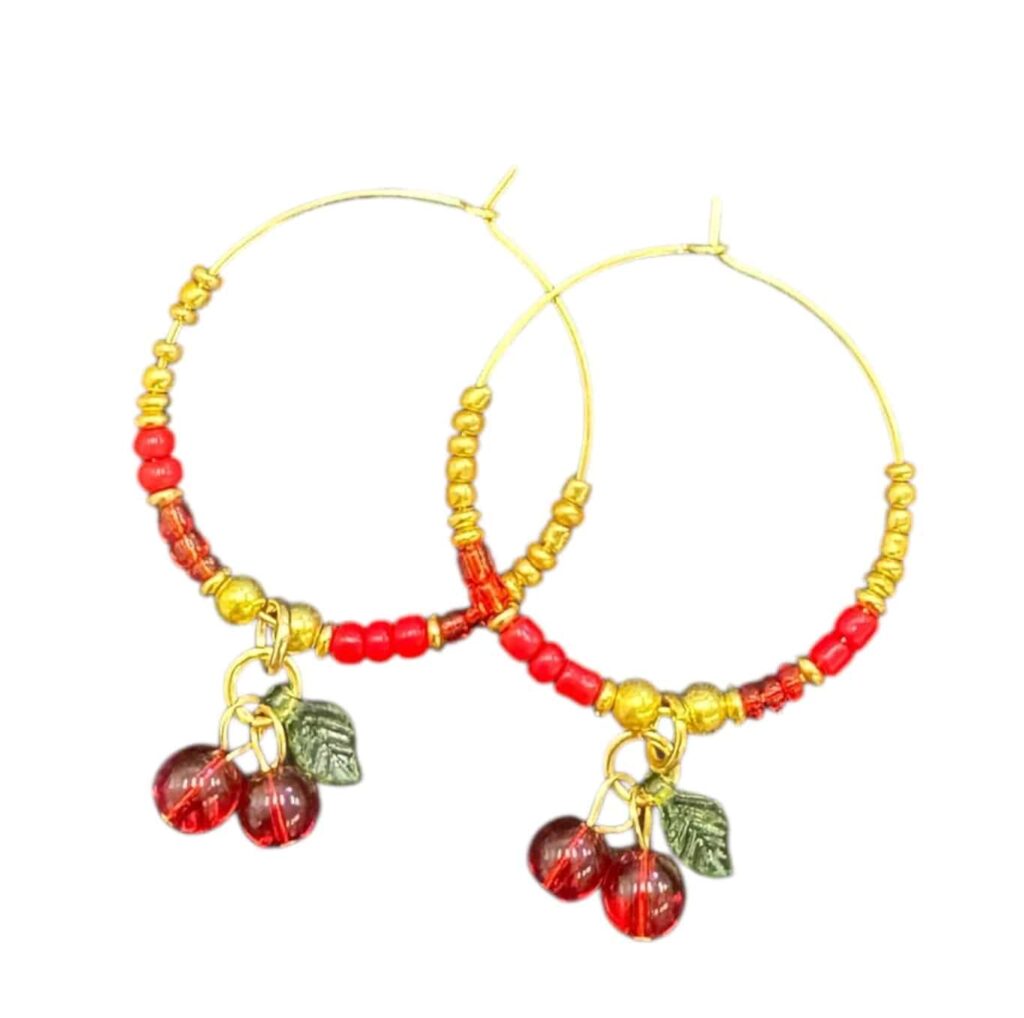 Playful and bold, the Cherry Bomb Hoops by Art in Stone feature glass cherry charms on gold hoops — handmade fun for fruit lovers.